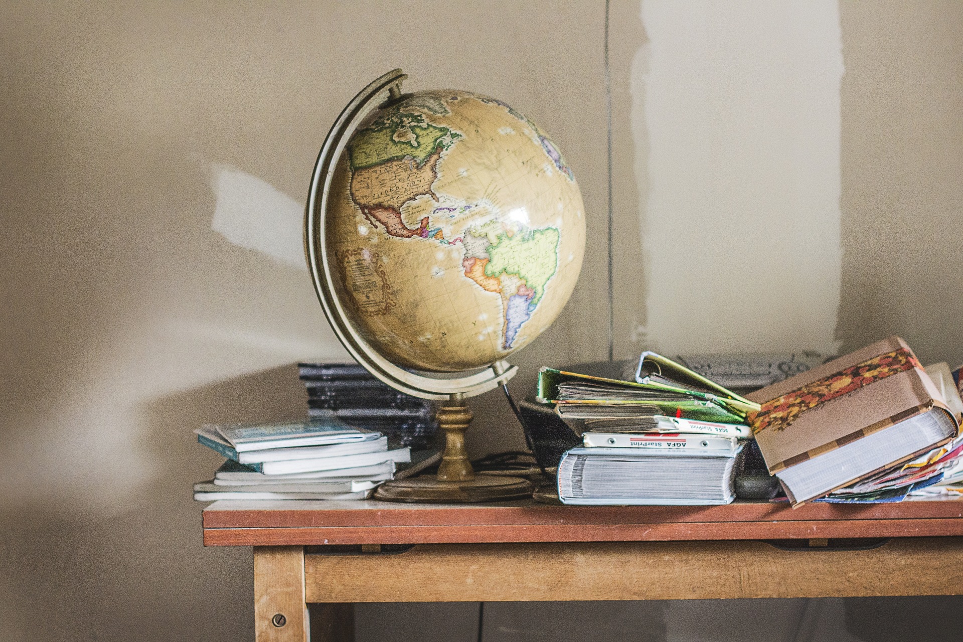 globus oraz książki leżące na brązowym drewnianym biurku